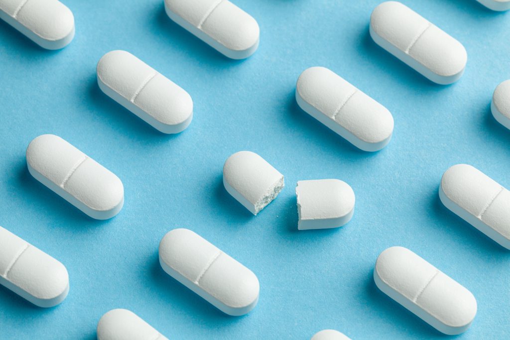White tablets on blue background. One tablet is broken in half, reducing the dose of the medicine
